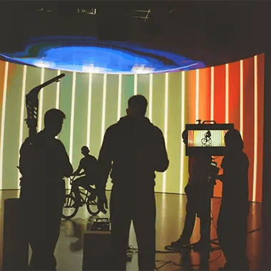Camera operator, director and first AC standing in front of an LED wall on a film set