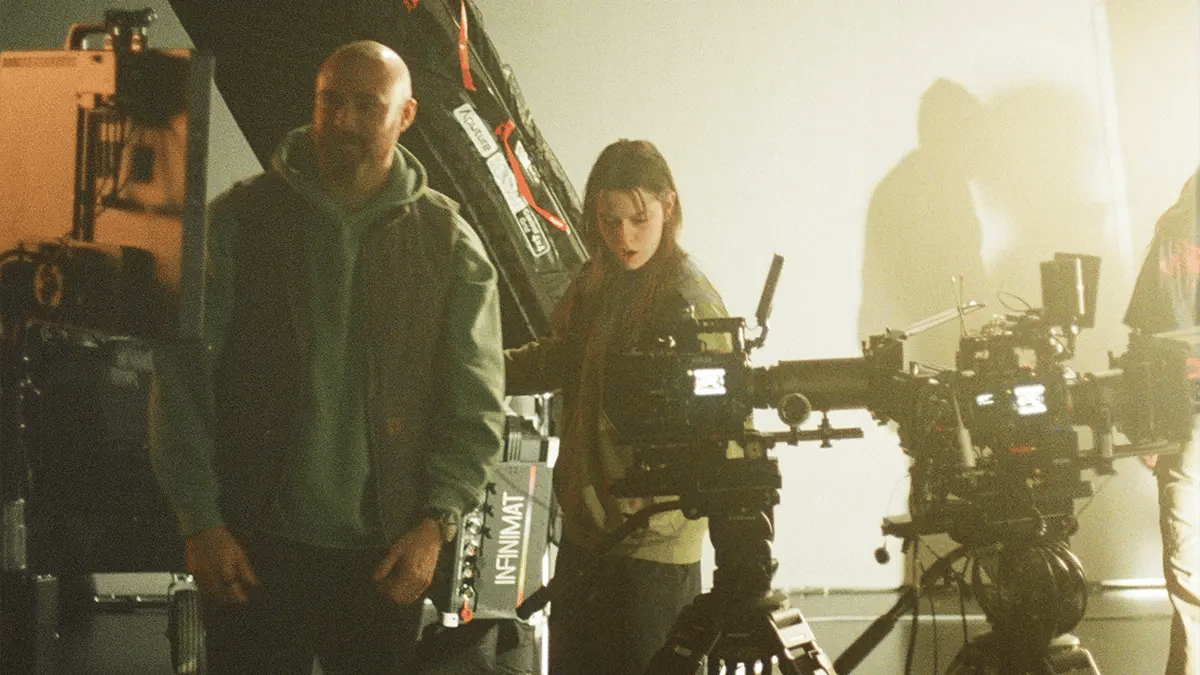 A cinematographer and camera operator stand together on a film set with cameras
