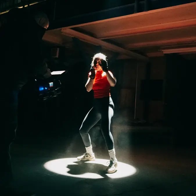 A boxer throws punches, highlighted by a spotlight while a cinematographer operates a RED cinema camera