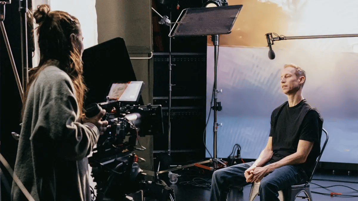 A man is being interviewed by a film crew while a camera operator uses a RED cinema camera