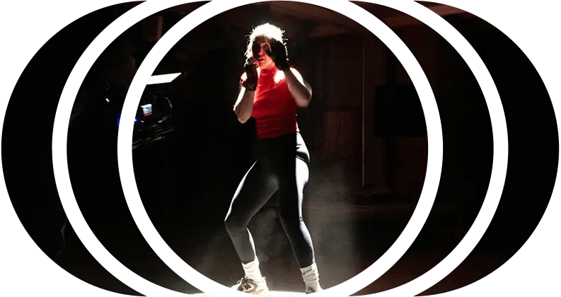 A boxer stands in a spotlight throwing punches while being filmed by a RED cinema camera