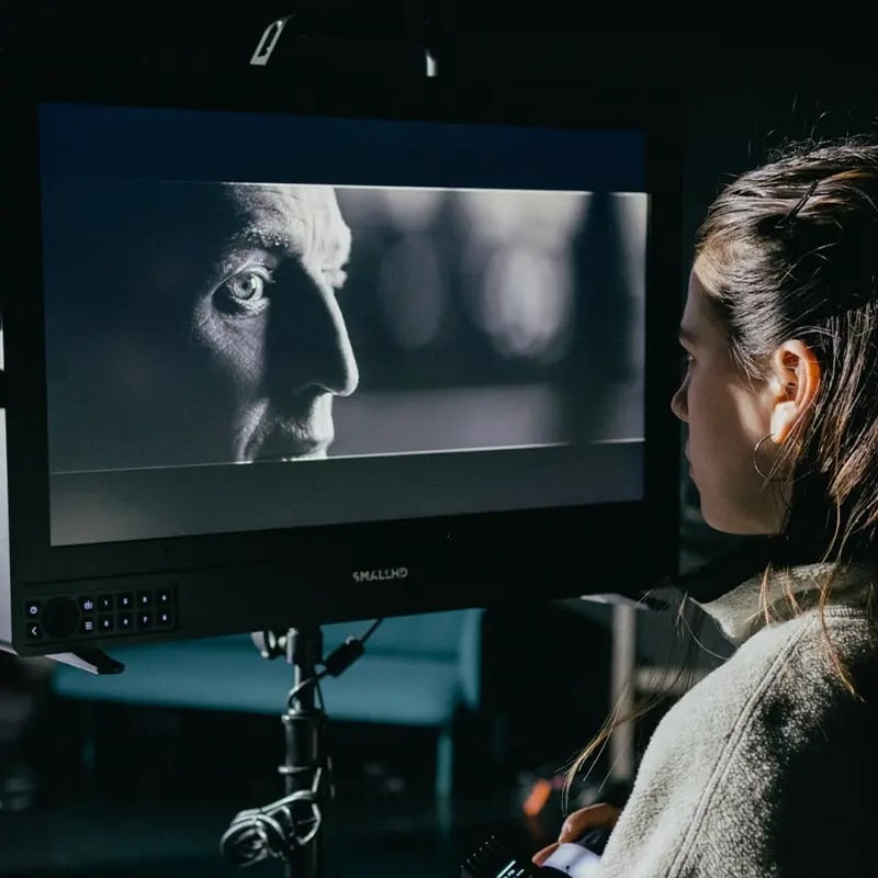 Film crew inspecting monitor showing a closeup of a man in black and white.