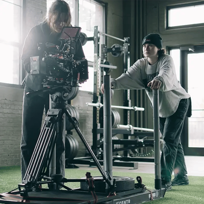A camera crew sets up a RED cinema camera on a weight sled at a gym to film athletes working out