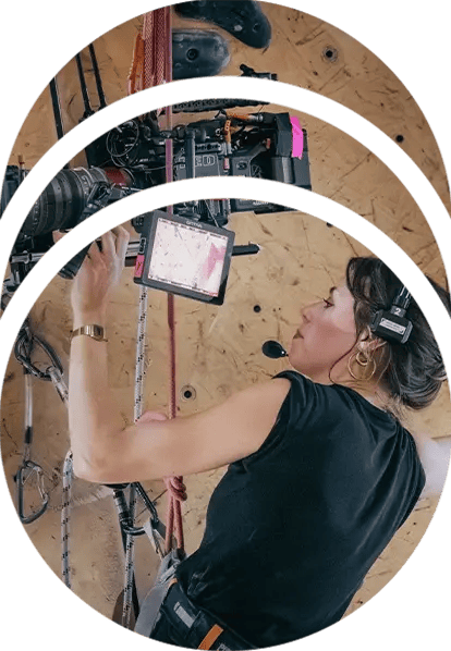 A camera operator operates a RED cinema camera while suspended on a rock wall at a climbing gym